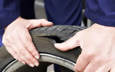 Dłonie mechanika pokazują oponę z dużym pęknięciem z boku. Widać wewnętrzną strukturę opony.