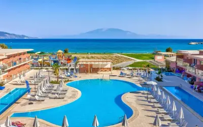Słoneczny dzień w Alykanas Beach Hotel. Baseny, zjeżdżalnie wodne i leżaki czekają na gości. W tle błękitne morze i góry.