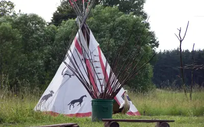 Wioska indiańska na Mazurach z tipi ozdobionym zwierzętami, bocianem i łukami.