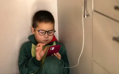 Chłopiec w okularach i piżamie z dinozaurem skupiony na telefonie. Czas na ekranie to wyzwanie, ale warto pamiętać o ograniczeniu czasu na telefonie.