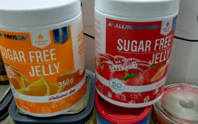 Dwie puszki galaretki bez cukru: pomarańczowa i truskawkowa. Zastanawiasz się, ile kalorii ma galaretka truskawkowa? Te produkty są niskokaloryczne.