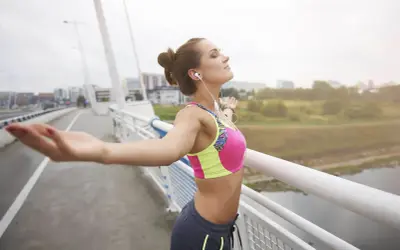 Kobieta w sportowym stroju na moście, z rękami rozłożonymi na boki, oddycha głęboko. To nie są objawy przemęczenia, lecz ulga po wysiłku.