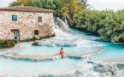 Cascate naturali con acqua turchese, una donna seduta su una roccia. Un antico mulino in pietra sullo sfondo. Tra le terme più belle d'Italia.