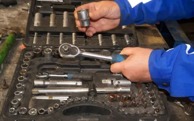Wybieranie odpowiednich rozmiarów grzechotek z walizki narzędziowej. Ręce mechanika w niebieskim kombinezonie trzymają klucz i nasadkę.