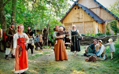 En grupp människor i vikingakläder samlas framför ett trädhus i vikingabyn Storholmen.