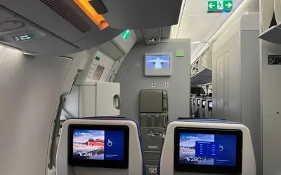 Blick in die Flugzeugkabine. Bildschirme zeigen "Lufthansa" und Sitzplatz 28B/C. Hier erfährst du, wo man im Flugzeug am besten sitzt.