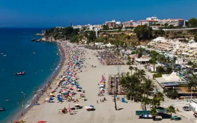 Vista aérea de la bulliciosa playa de Burriana, considerada la mejor playa de Nerja, con gente disfrutando del sol y el mar azul.