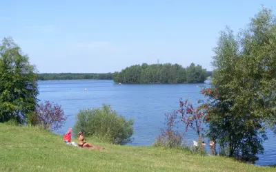 Słoneczny dzień nad jeziorem Chechło-Nakło. Kobieta odpoczywa na trawie, w tle błękitna woda i zielone wyspy.