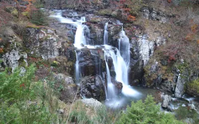 Il sentiero delle cascate serpeggia tra rocce e foliage autunnale, con l'acqua che scende impetuosa.