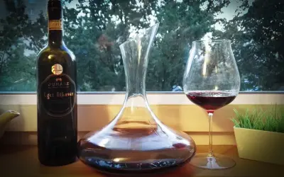 Butelka wina Egri Bikavér, karafka i kieliszek z czerwonym winem. Właściwości tego węgierskiego trunku są cenione przez koneserów.