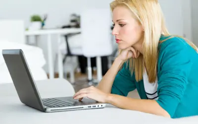 Kobieta z blond włosami pracuje na laptopie, analizując dokumenty dotyczące spłaconego komornika i kredytu hipotecznego.