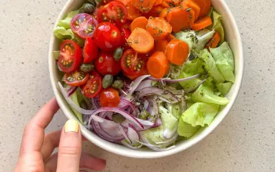 Deliciosa ensalada mediterránea con lechuga, tomates cherry, zanahoria, cebolla morada y alcaparras.