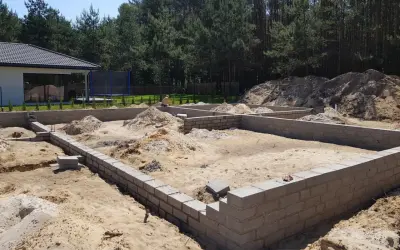 Fundamenty domu w budowie. Piasek, bloczki betonowe i kopce ziemi. To pierwszy krok, od czego zacząć budowę domu.