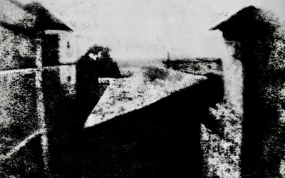 Widok z okna, jeden z pierwszych fotografii. Dachy i budynki w szarościach.