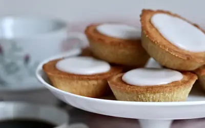 Små, gyllene mazariner med vit glasyr på ett tårtfat. Perfekt till fikat, här är ett enkelt mazariner recept.