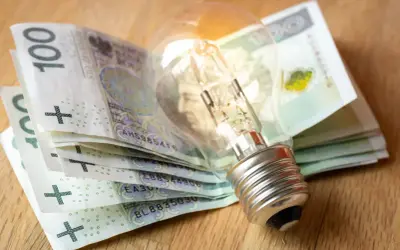 Żarówka na stosie banknotów 100 zł. Zastanawiasz się, jak dostać dofinansowanie do prądu?