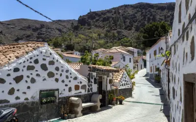 Urocza uliczka z białymi domami i kamiennymi detalami, idealna na gran canaria plan zwiedzania. W tle góry.