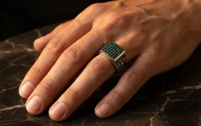 Anillo de plata con piedras verdes, puesto en el dedo anular, el dedo en que se pone un anillo normal.