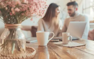 Un couple discute devant un ordinateur portable, entouré de tasses et de fleurs roses. Ils planifient leur préparatif mariage.