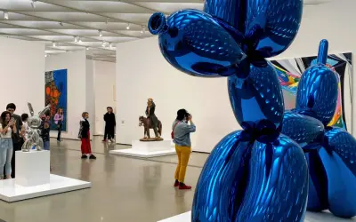 Visitors admire a giant blue balloon dog sculpture in a modern art gallery, a highlight among the top art galleries in the world.