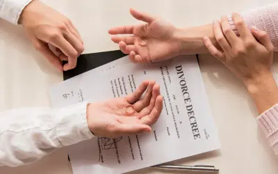 Dwie dłonie trzymają obrączki na tle dokumentu "DIVORCE DECREE". Zastanawiasz się, jak napisać papiery rozwodowe?