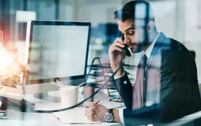 Biznesmen w garniturze rozmawia przez telefon, notując. Czasem nawet siła wyższa nie przeszkodzi w pracy.