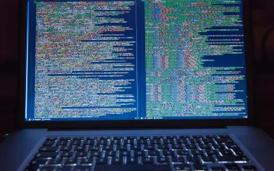 Programista pracuje nad kodem. Na ekranie laptopa widać wiele linii kodu, co pokazuje, co robi programista.