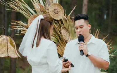 Un homme prononce un discours de mariage devant une femme voilée, micro en main, lors d'une cérémonie en plein air.