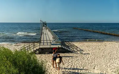 Sianożęty atrakcje: drewniane molo na plaży, ludzie spacerują, morze i niebo.