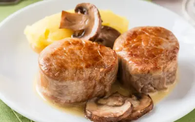 Dwie soczyste polędwiczki wieprzowe pieczone w piekarniku, podane z puree ziemniaczanym i pieczarkami.