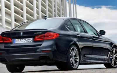 Ciemny BMW m550i z napędem xDrive, z widocznym logo BMW i oznaczeniem modelu, zaparkowany przed nowoczesnym budynkiem.