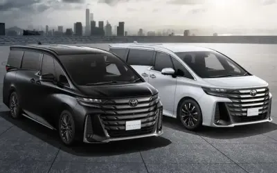 Dwa luksusowe minivany Toyota Vellfire, czarny i biały, prezentują się na tle miejskiej panoramy.