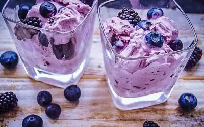 Zwei Gläser mit cremigem, lila gefärbtem frozen joghurt, garniert mit frischen Blaubeeren und Brombeeren.