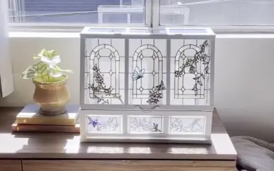 Boîte à bijoux ornée de vitraux décoratifs représentant des papillons et des fleurs, posée sur une commode en bois.