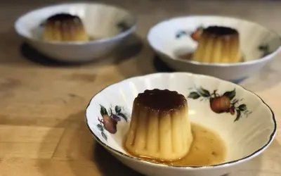 Tre krämiga creme caramel i vackra skålar med fruktmotiv. En härlig dessert som väntar.