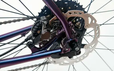 Błyszcząca, fioletowa rama roweru z widoczną sztywną osią w rowerze, hamulcem tarczowym Shimano i kasetą.