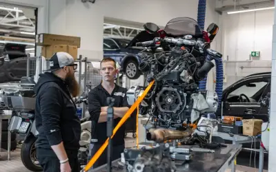 Mechanicy omawiają regulację linki sprzęgła przy silniku motocykla wiszącym na taśmach.