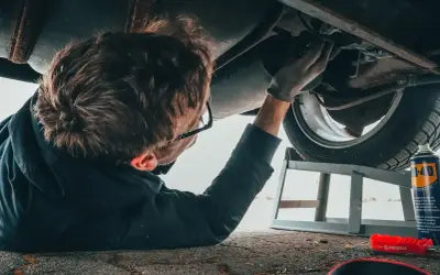 Mechanik pod samochodem, zastanawia się ile zarabia diagnosta samochodowy.