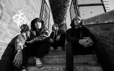 Tre uomini con cappuccio siedono sulle scale, un'atmosfera da musica hip hop famosa.
