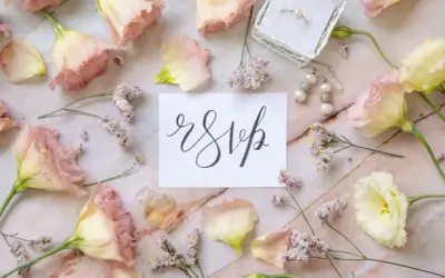 Delikatne kwiaty i biżuteria otaczają kartkę z napisem "rsvp".