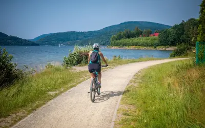 Kobieta na rowerze przemierza malowniczą ścieżkę nad jeziorem. Idealne miejsce, gdzie na rower!