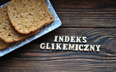 Plasterki chleba pełnoziarnistego na talerzyku z niebieskim wzorem. Obok drewniane litery układają się w napis "INDEKS GLIKEMICZNY".