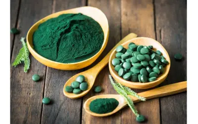 Chlorella vs spirulina: zielony proszek i tabletki na drewnianym tle. Dwa rodzaje alg w formie suplementów diety.