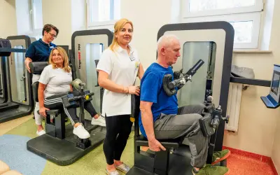 Rehabilitacja w Busko Zdrój: pan ćwiczy na siłowni pod okiem fizjoterapeutki, a pani z pomocą drugiej terapeutki. Sprawdź nasze sanatoria Busko Zdrój promocje!
