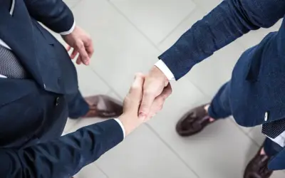 Dwaj mężczyźni w garniturach ściskają sobie dłonie na jasnej posadzce.