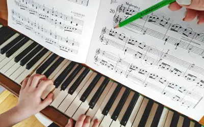 Dziecko uczy się grać proste melodie na pianino. Zielony ołówek wskazuje nuty w zeszycie.