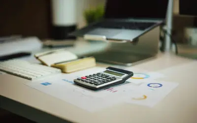 Kalkulator na biurku obok laptopa i notatnika. Czy to już czas na podsumowanie, co netto?