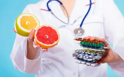 Lekarz trzyma połówki grejpfruta i pomelo, ostrzegając przed popijaniem leków sokiem grejpfrutowym.