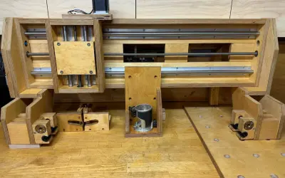 Domowa frezarka CNC DIY z drewna i metalowych prowadnic. Widać silnik krokowy, wrzeciono z frezarką ręczną i mechanizm śrubowy.
