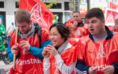 Junge Leute in roten Westen mit IG Metall Logo bei einer Demonstration. Sie wirken engagiert und hoffnungsvoll für die jav Wahlen.